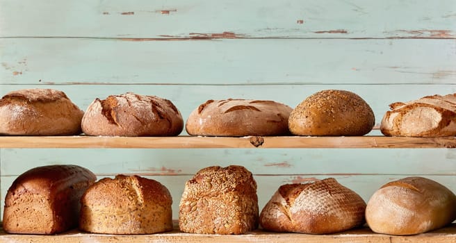 Assorted freshly baked loaves of crispy bread with crispy crust placed on shelves against shabby wooden background in light studio