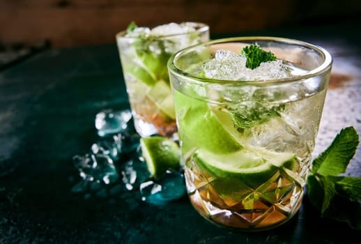 Glasses of refreshing alcoholic cold mojito cocktails with lime wedges and ice cubes served on table with fresh mint leaves