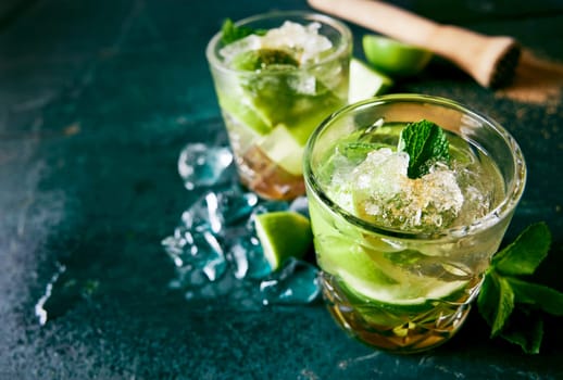 From above of glasses filled with refreshing caipirinha drinks with ice cubes and lime placed on dark wet table