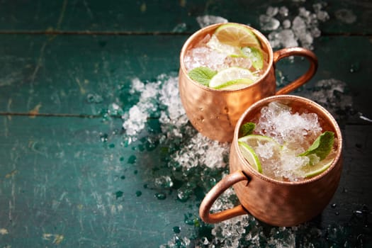 From above of alcoholic Moscow mule beverages with lime slices and ice served in copper mugs on shabby wooden table
