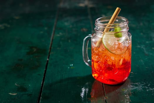 Glass jar filled with refreshing sweet red berry beverage served with lime and straw on dark wooden table