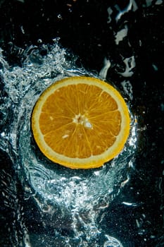 From above round slice of tasty ripe orange on water surface with splashes and water drops in modern light studio