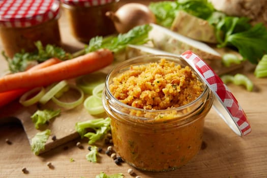 Glass jar with tasty vegetable conservation for soups and sauces on wooden table with various raw ingredients in light kitchen