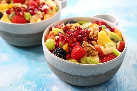 Mix of chopped ripe tasty fruits and berries topped with pomegranates and walnuts served in bowl on table in light kitchen