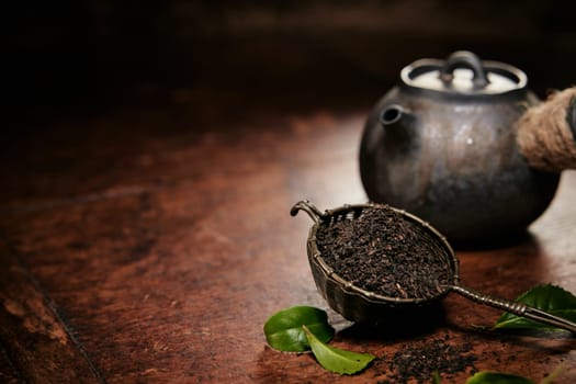 Aromatic loose tea fro brewing in metal ladle placed on table with leaves and old fashioned metal teapot in kitchen