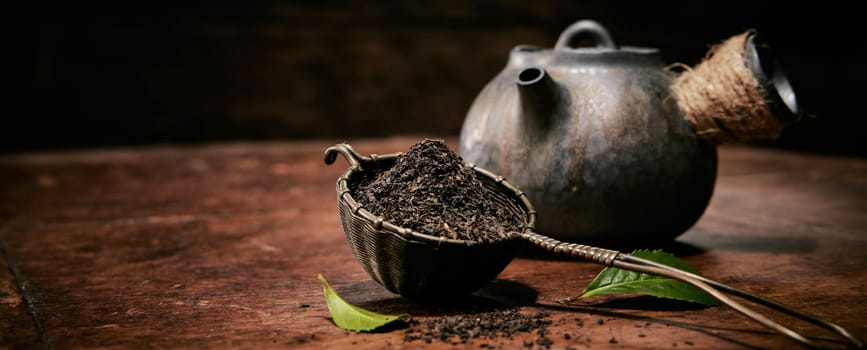 Heap of loose tea on table with fresh green leaves for brewing placed on wooden table with vintage metal teapot