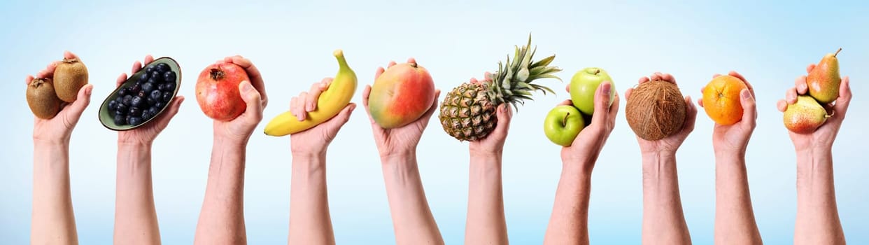 Hands of crop anonymous people holding mix of ripe tasty colorful exotic fruits and berries against light background in studio