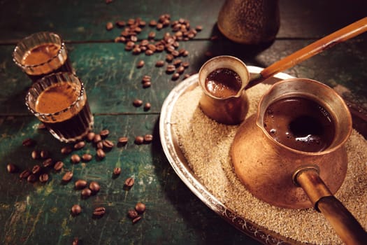 From above cezves on sand and glasses with hot traditional oriental coffee placed on table with scattered coffee beans in kitchen