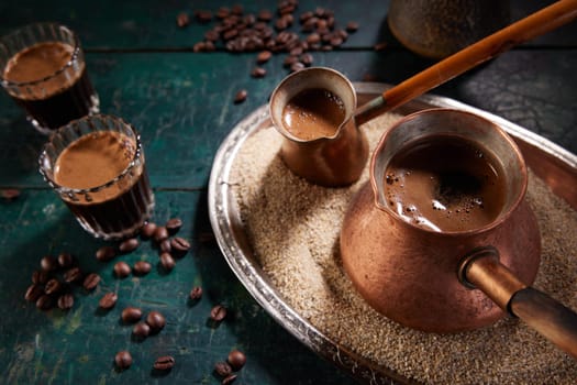 From above of metal cezves filled with freshly brewed aromatic hot oriental coffee on sand placed on table with glasses