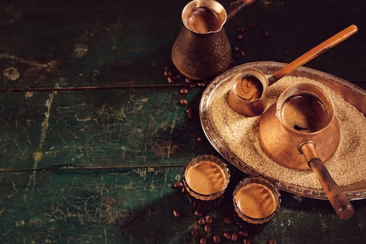 High angle of tasty freshly brewed Turkish coffee in cezves and glasses placed on weathered green wooden table in kitchen