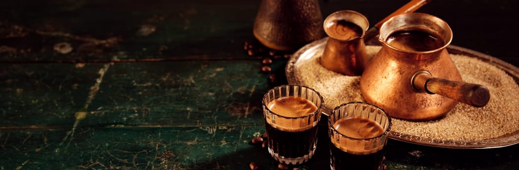 Metal cezves on tray with sand and glasses filled with hot aromatic oriental coffee served on shabby table in kitchen