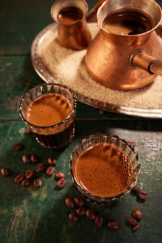 From above of authentic Turkish coffee in glasses and cezves on sand placed on wooden table in kitchen during break