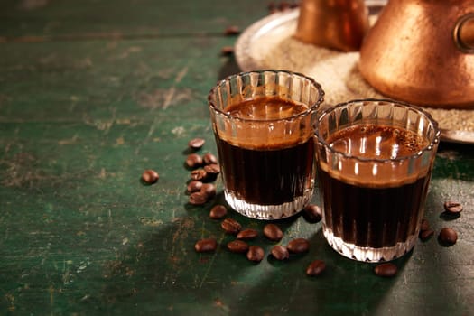 Glasses filled with traditional tasty Turkish coffee placed on shabby wooden table near copper cezves in light kitchen during coffee break