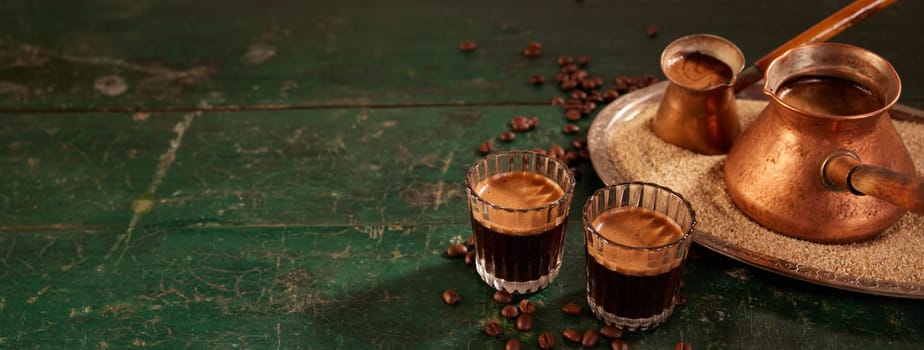 Glasses and cezves on sand with tasty freshly brewed coffee with froth placed on shabby green wooden table in kitchen
