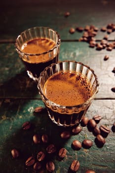 From above of traditional Turkish coffee with froth placed on weathered wooden table with scattered beans in kitchen during break