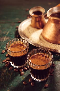 From above of Turkish hot coffee in glasses and cezves placed on shabby wooden table with scattered coffee beans in kitchen during break