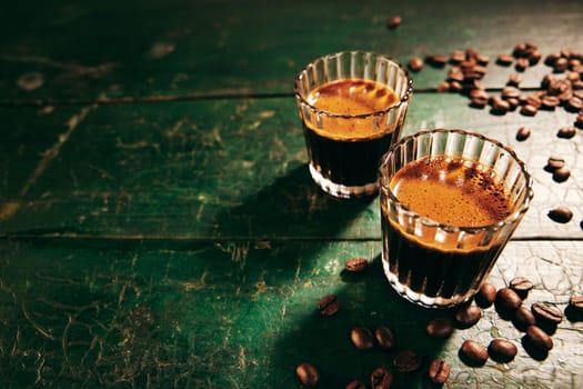 From above of traditional oriental freshly brewed coffee in glasses placed on wooden shabby table with scattered beans in kitchen