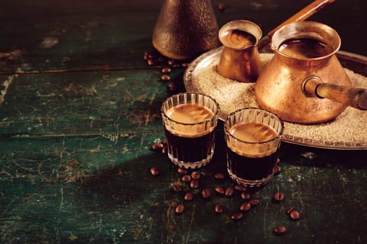 High angle of traditional hot oriental coffee in glasses and metal cezves served on weathered green wooden table in kitchen