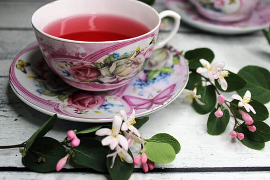 A cup of tea on a wooden table with a background of white and pink flowers..