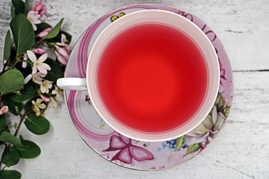 A close-up cup of tea on a wooden table with a bouquet of white and pink flowers. Top view..