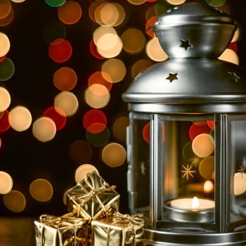 Christmas composition: a lantern with candles, bright shiny boxes with gifts, blurred bokeh lights in the background.