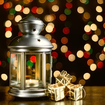 Christmas composition: a lantern with candles, bright shiny boxes with gifts, blurred bokeh lights in the background.