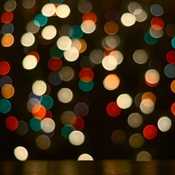 Festive background. A dark table and blurry multicolored lights in the background.