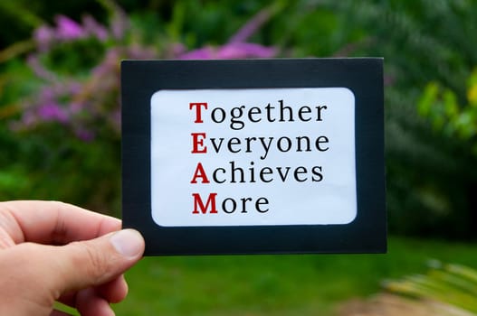 Hand holding notepad with text - TEAM. Blurred nature background. Teamwork concept