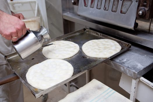 Elaboration process of traditional spanish olive oil pancakes. Baker fills with oil the holes of raw bread prior baking
