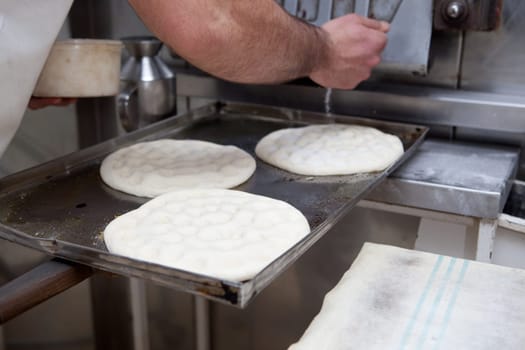Elaboration process of traditional spanish olive oil pancakes. Baker fills with sugar the holes of raw bread prior baking