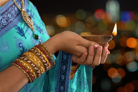 Diwali or festive of lights. Traditional Indian festival, woman in sari hands holding oil lamp, copy space at side.