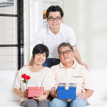 Asian senior parents receiving gift from their child. Family at home.