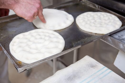 Elaboration of traditional spanish olive oil pancakes. Baker making holes on raw bread using his finger to shape the dough prior baking