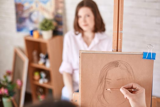Human hand with crayon drawing young woman in studio