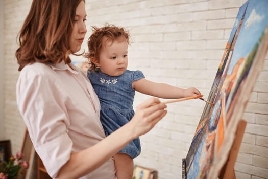 Young mother teaching her cute little daughter how to paint