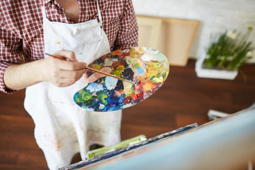 Close-up of artist hands with paintbrush and palette mixing water-colors