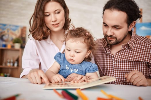 Young parents and their small daughter reading together
