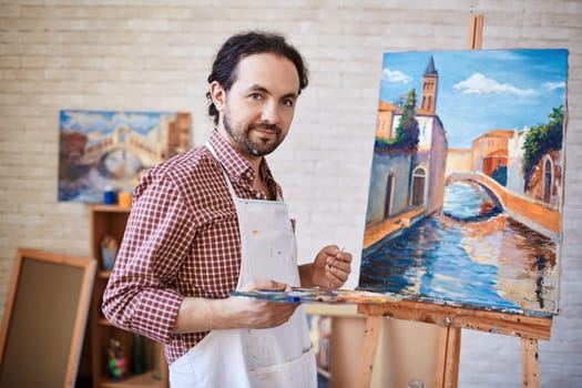 Young artist looking at camera on background of his painting