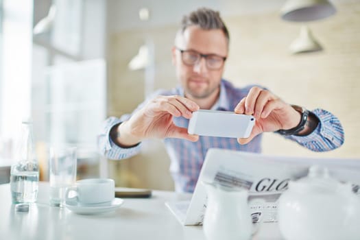 Businessman using smartphone to take photo of something in newspaper
