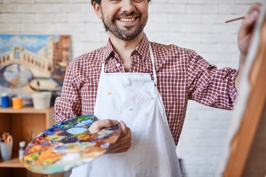 Happy artist holding palette with mixed colors while painting