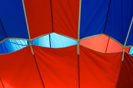Close up of straps holding bottom of hot air balloon to the top making an abstract red and blue image.