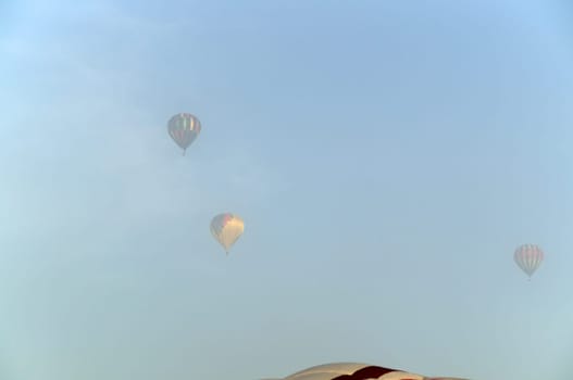 Three hot air balloons can be seen high up in the sky and partially obscured by the fog in the air, the top of another can be seen in the bottom of the image.