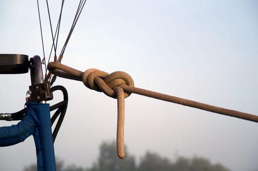 A strong rope is tied to the cables of a hot air balloon to hold it to the ground on a foggy morning. Balloon is not shown.