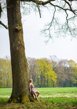 Young woman in summer dress leans against a tree