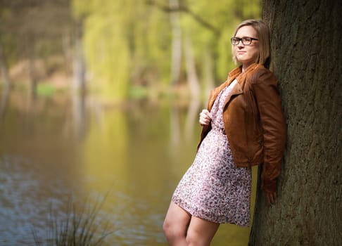 Young woman in spring leans against a tree trunk