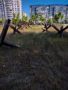 Iron anti-tank structures on the background of city buildings. War in Ukraine. Martial law in the city of Kyiv. Anti-tank military barricade on the city street.