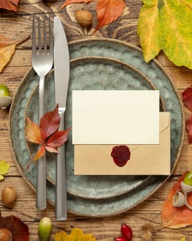Autumn rustic table setting with blank place card and envelope between colorful leaves and berries, top view, mockup. Flat lay Horizontal card on wooden table, flat lay, copy space. Thanksgiving or harvest