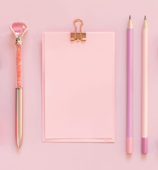 Pink paper card with a clip, pensils and decorative gemstone pen on light pink top view. Textbook mockup, planner cover with place fot text. Educational and girly concept