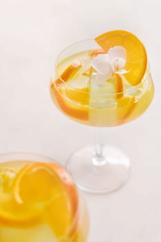 Transparent cocktail with ice cubes in a champagne coupe glass decorated with slices of orange close up. Tropical drink at the bar. Summer vacation mood