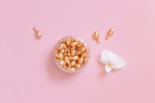 Beauty serum capsules in a jar near orchid flower on light pink top view. Skincare beauty product. Facial cosmetics, pastel minimal composition..
